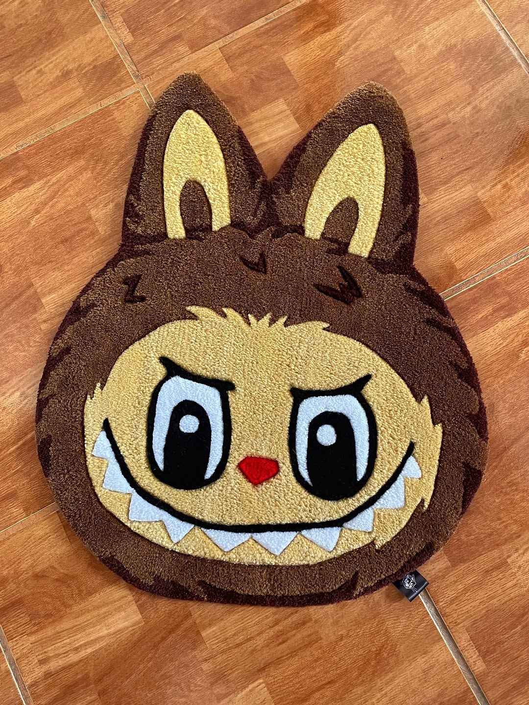 Labubu area rug with dark brown face, yellow eyes, and red nose