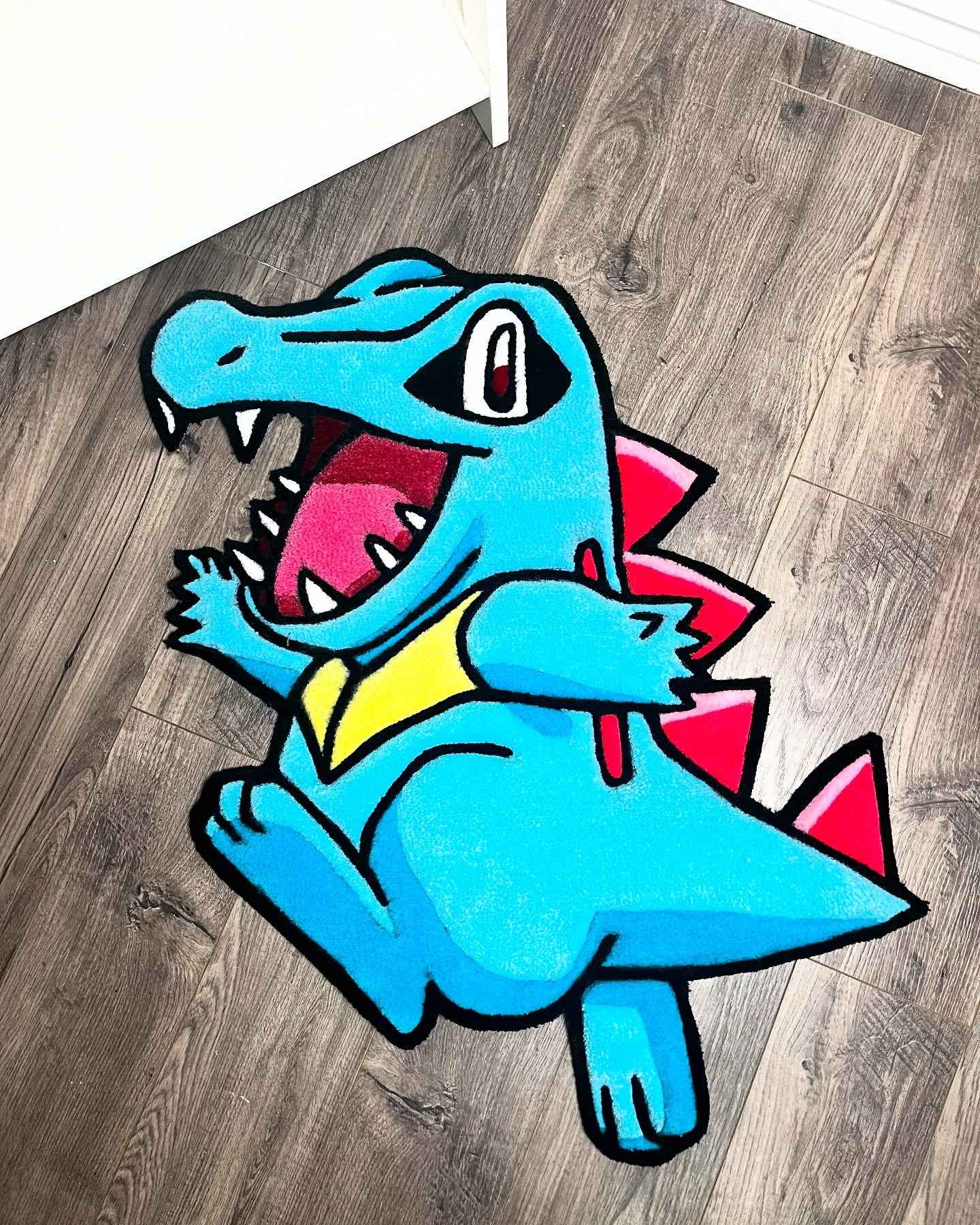 Tufted rug showing a blue water starter character sitting, with red and yellow details